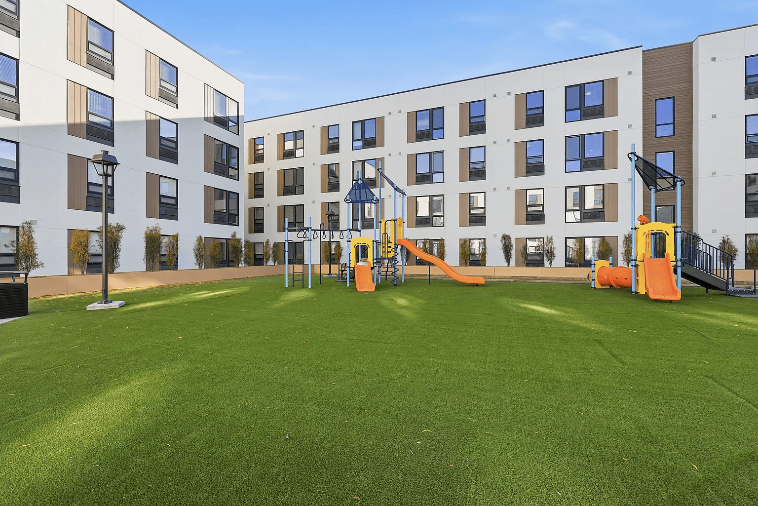 A playground with a slide and a green lawn in front of apartment buildings.